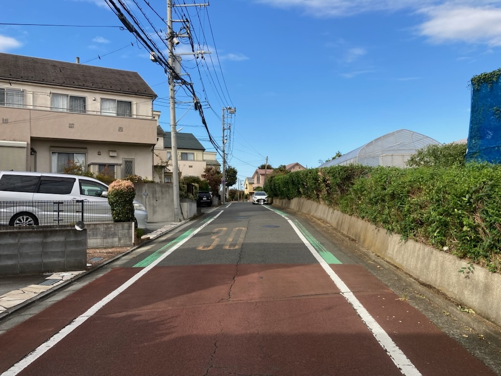 【現地土地写真】 分譲地内の前面道路は幅員約5.0m〜約6.0m。高層建築物のない、第1種低層住居専用地域内に位置しているため、落ち着いた暮らしが叶います。/2025年11月撮影